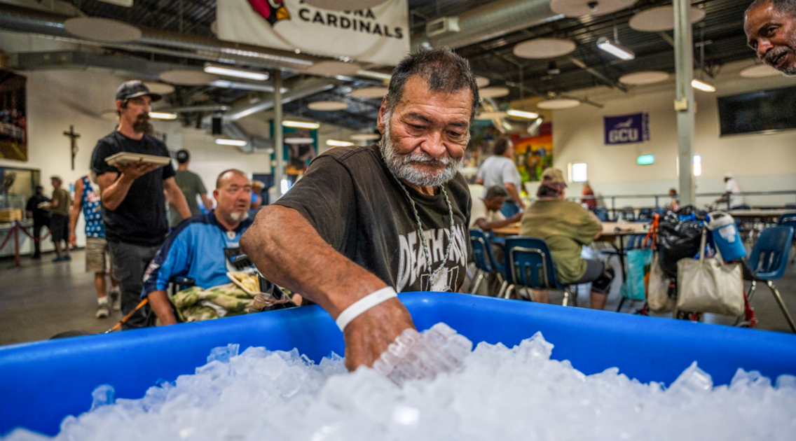 A man experiencing homelessness grabbing a bottle of water from the distribution bucket.