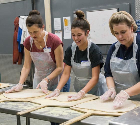 Three women stretching out pizza dough