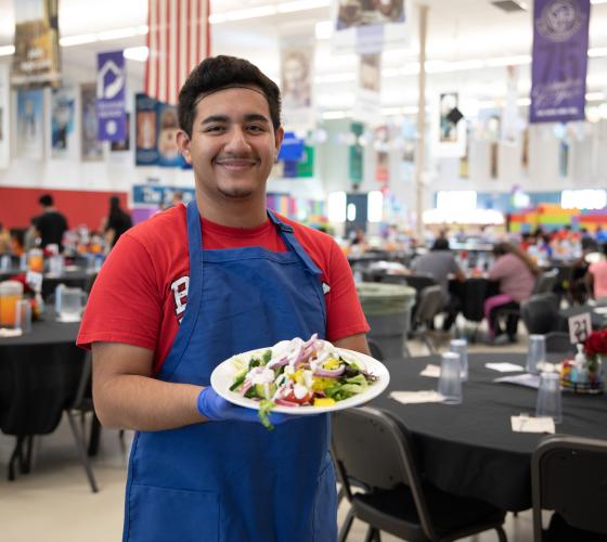 Young man standing in a dining room holding a plate of vegetables