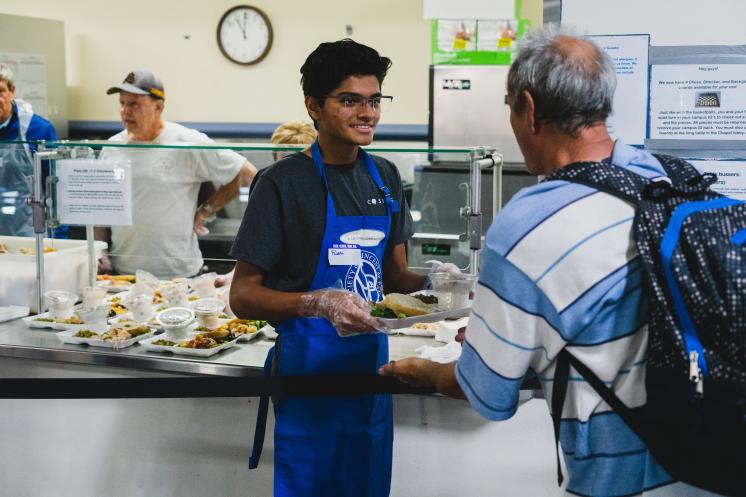 Dining Rooms VSO Header Young man handing a tray of food to an older man