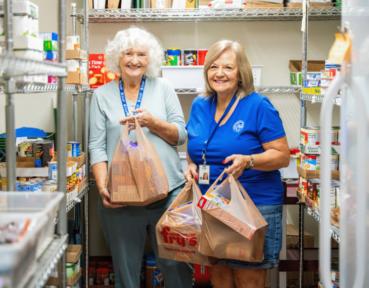 Two Vincentian volunteers in a food pantry holding bags of food preparing for a home visit.