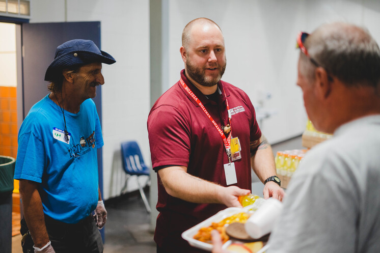 Arizona State University volunteer at Phoenix Dining Room serving meal and drinks to visitor.