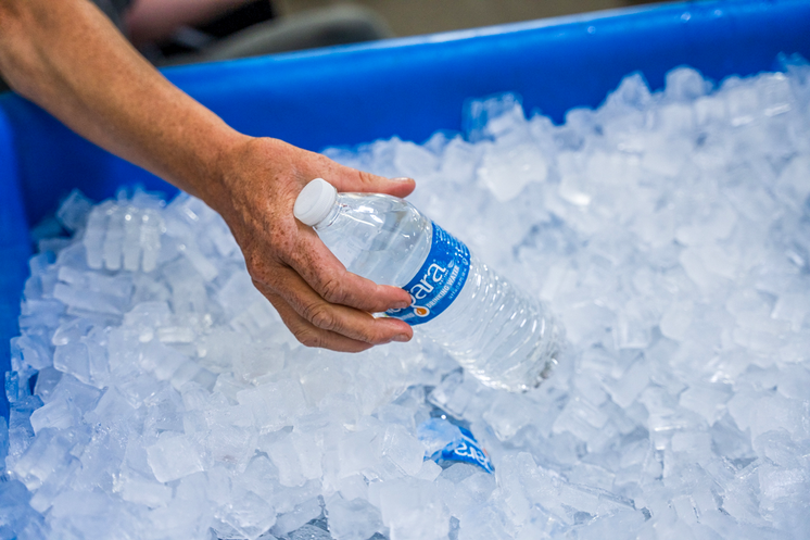 A hand reaching in a water distribution bucket to pick up a bottle of water.