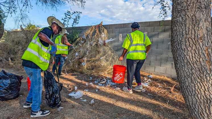 Members of the neighborhood brigade picking up trash out of a bush