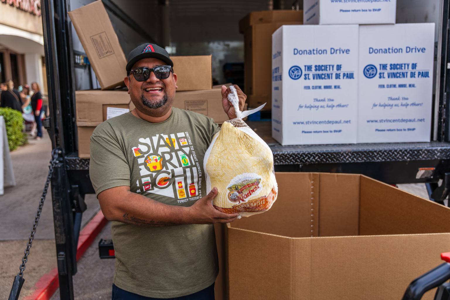 turkey-tuesday-fundraiser-header Man standing next to a box holding a turkey and smiling
