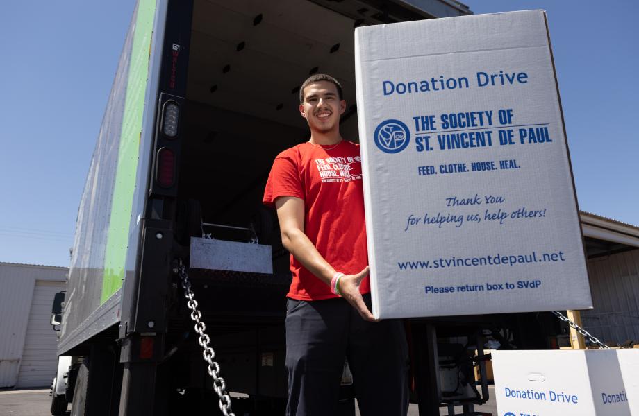 Man standing on the bed of a large truck holding a box