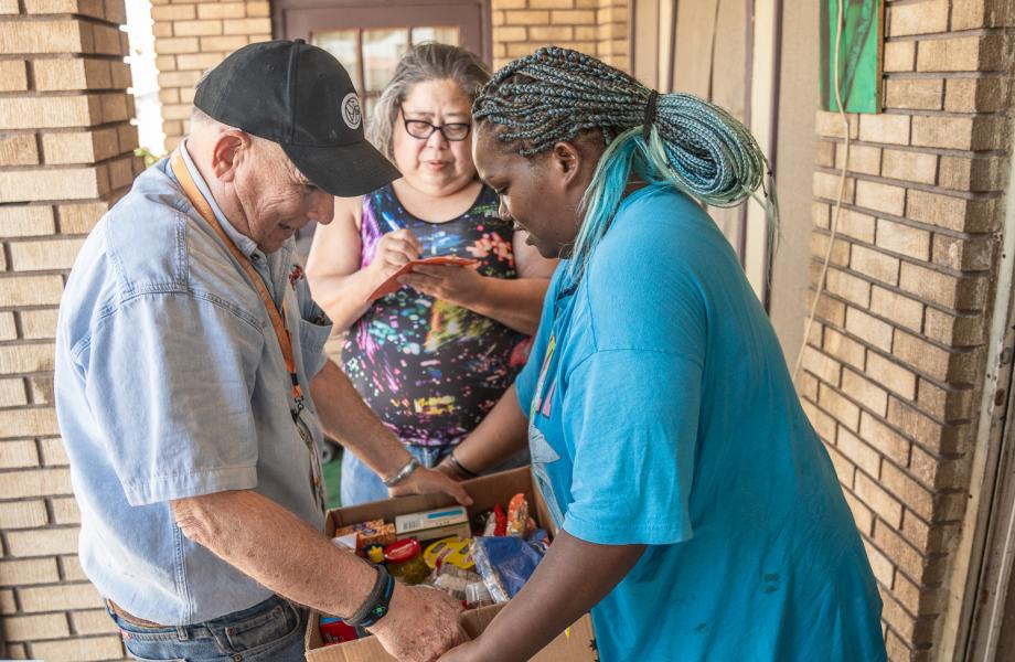 Bill, a Vincentian volunteer, hands Katherine a food box as her mother, Sandra, fills out a form in the background.