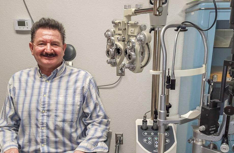 Francisco sits in a medical clinic chair with the optometrists instruments next to him.