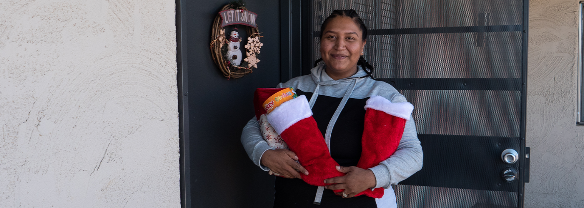 christmas-campaign-header Woman standing in front of her apartment holding two stuffed stockings