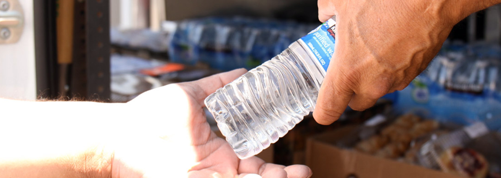 water-campaign-header person handing a bottle of water to another person