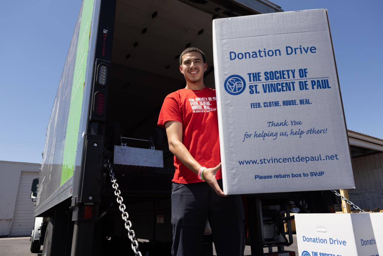 Man standing on the bed of a large truck holding a box