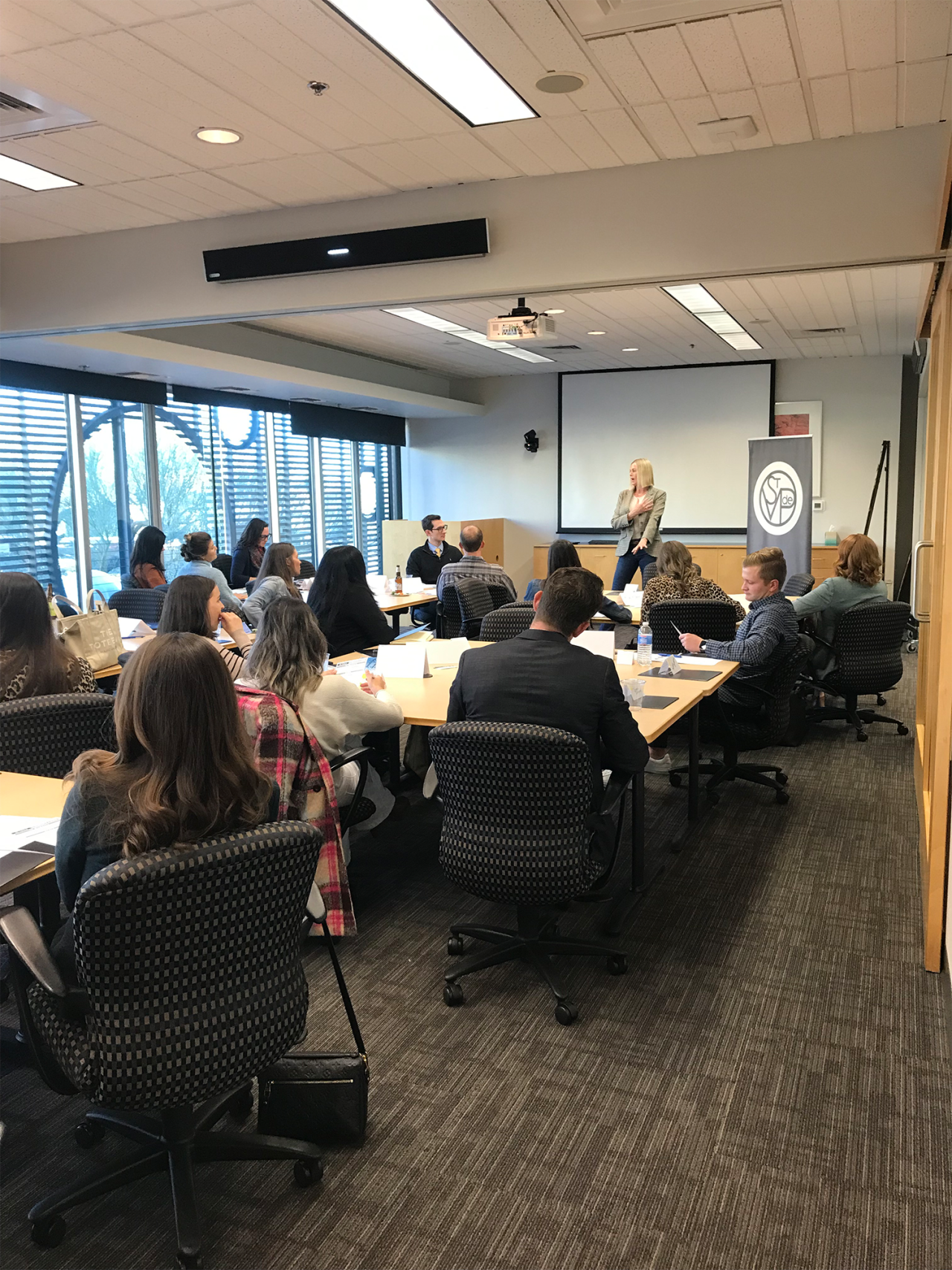 woman speaking to a conference room full of young professionals