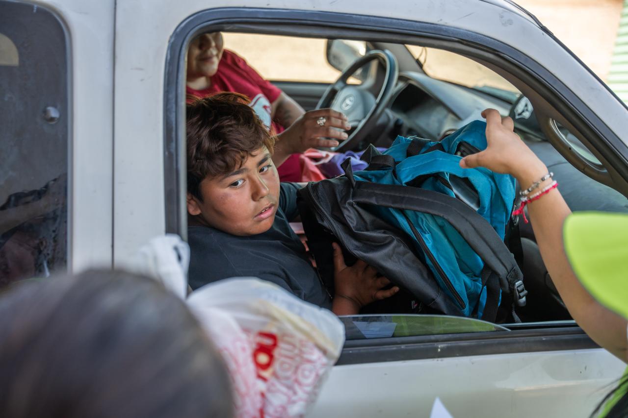 A kid in a vehicle receives backpacks from SVdP volunteers.