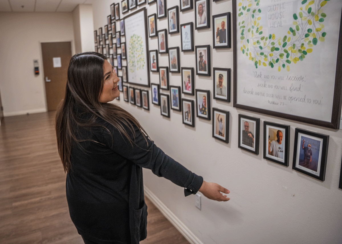 Case manager Emily Perales showcases the wall of graduated Ozanam Manor residents proudly holding up their keys to their new, permanent homes.